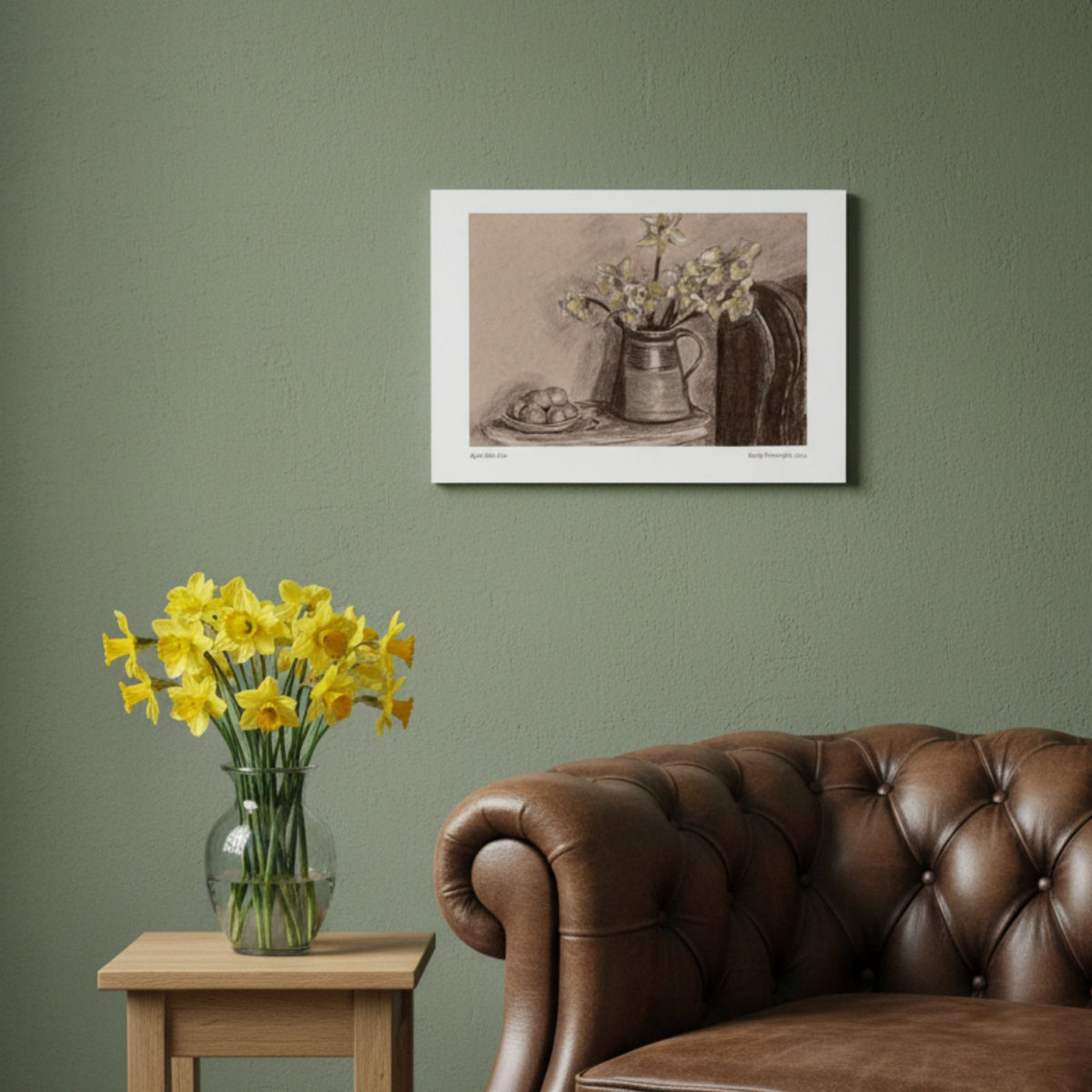 A sepia-toned still life art print depicting a vase of flowers and a bowl of eggs, hanging on a green wall in a styled room with a leather armchair and vase of daffodils