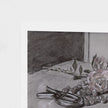 A square art print featuring a charcoal and pencil still life sketch of roses, nuts, and a stem on a table, shown with a white border against a textured off-white background.
