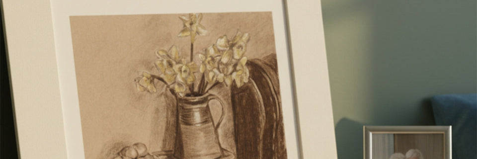 A framed still life drawing of yellow daffodils in a brown pitcher, shown leaning against a wall in an indoor setting.
