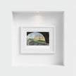 A framed art print depicting Biddulph Grange seen through a dark archway, displayed in a white frame on a white wall within a recessed niche.