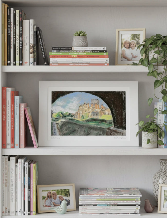 A mounted art print depicting Biddulph Grange through an archway, styled on a white bookshelf alongside books, small potted plants, and framed photos.