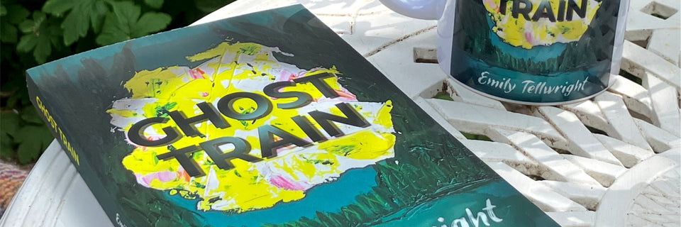 A book titled 'Ghost Train' by Emily Tollwright lies on a white slatted outdoor table next to a matching mug. The book cover features a dark teal background with a bright yellow and white paint-splatter graphic and bold black title text.
