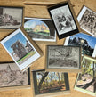 A collection of art greetings cards  arranged on a wooden table. The prints feature monochrome charcoal drawings, landscape scenes, and figures, with some showing visible wood frames.