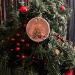 a round ceramic ornament showing a christmas tree hanging on decorated fir foliage