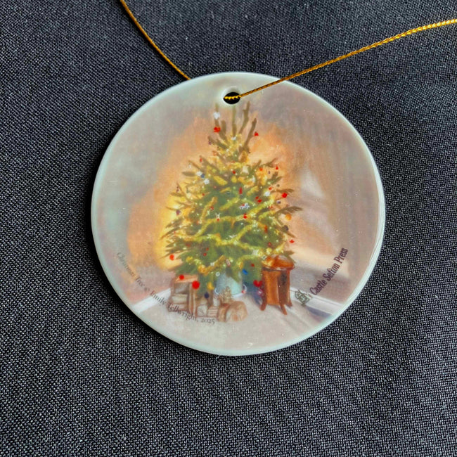 A round ceramic ornament showing a christmas tree with a hole threaded with a gold cord all on a black background