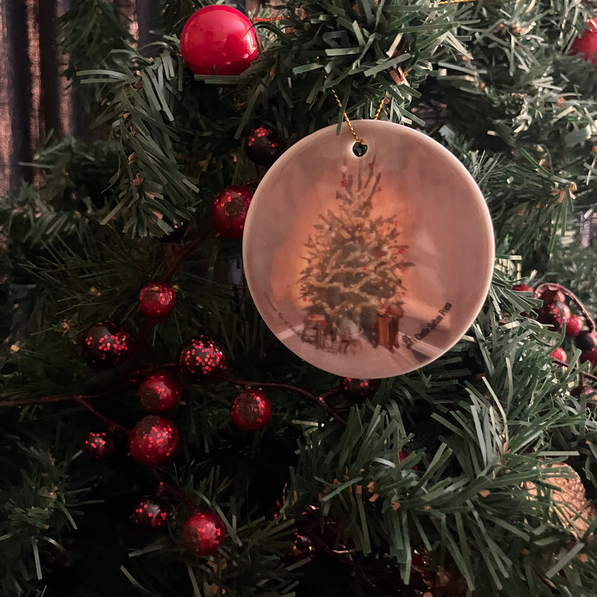 a round ceramic ornament showing a christmas tree hanging on decorated fir foliage