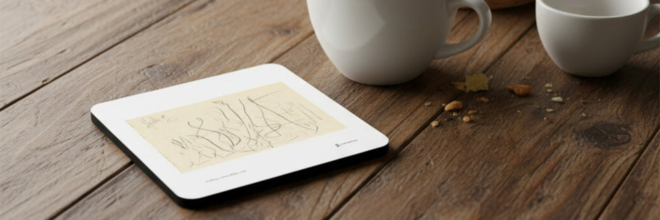 A white abstract art coaster on a wood table next to some coffee cups