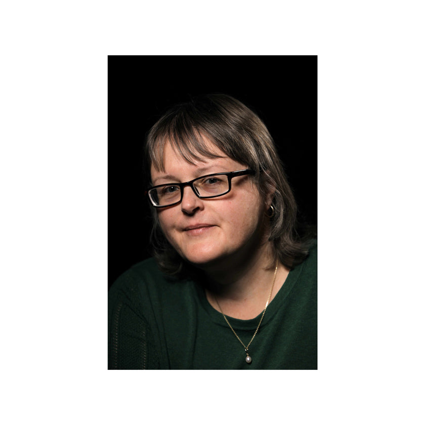 A portrait of a woman with short brown hair and glasses, wearing a dark green top against a black background, centered on a white canvas.