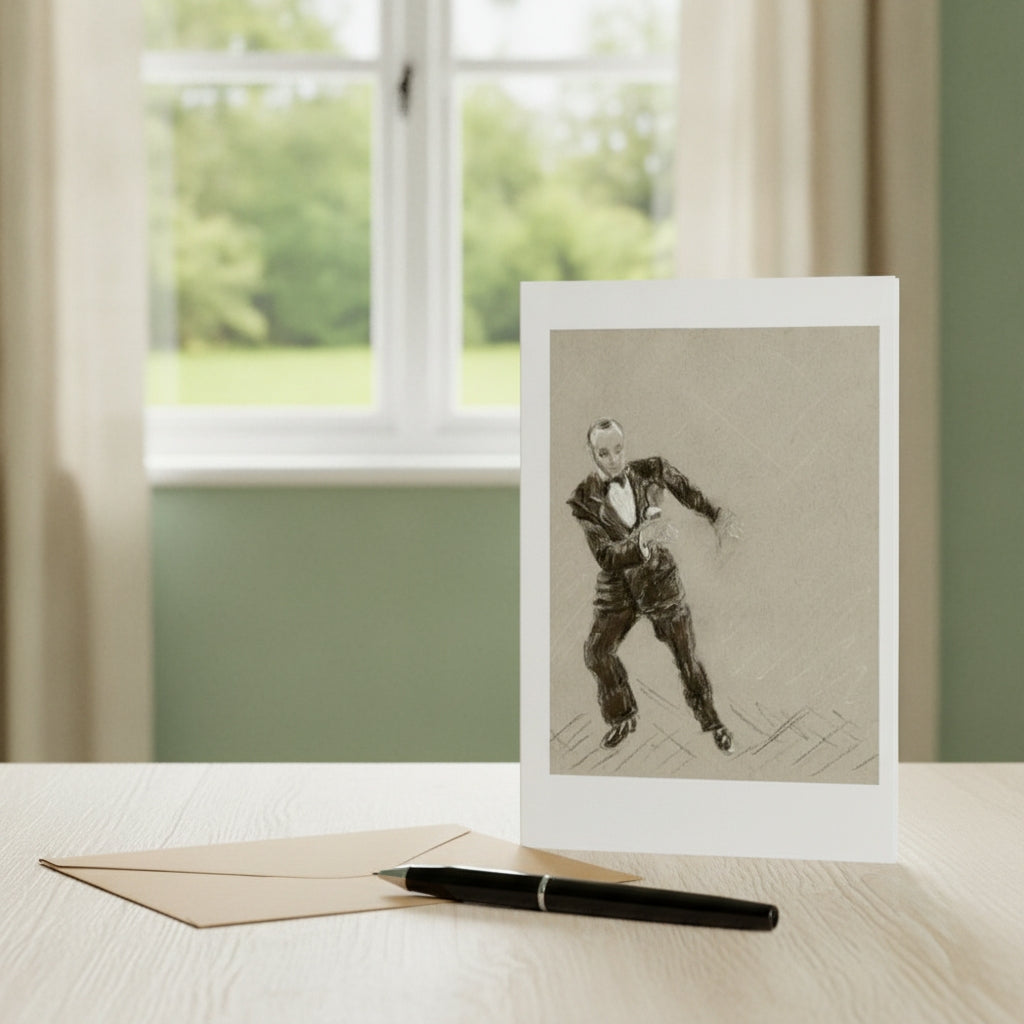 A greetings card featuring Fred astaire, displayed on a light wood table next to a gold envelope and a black pen, with a blurred window and green garden in the background.