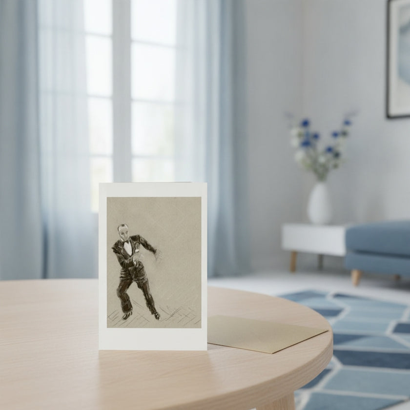 A greeting card with a white border stands on a light wood table in a softly blurred living room. The print shows a black and white sketch of Fred Astaire