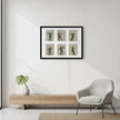 A framed wall art print showing six black silhouette dance poses on a beige background, hung on a white wall above a light wood console table and next to a grey armchair.