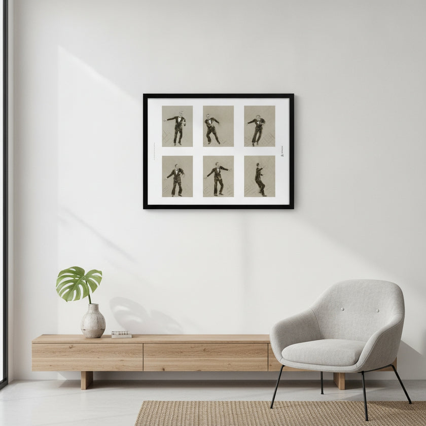 A framed wall art print showing six black silhouette dance poses on a beige background, hung on a white wall above a light wood console table and next to a grey armchair.