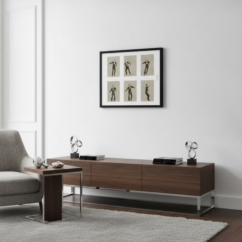 A modern living room scene featuring a dark brown wooden media console with silver metal legs, styled with decorative objects. Above it, a black-framed art print depicting six black-and-beige dance or gymnastic poses hangs on a white wall.