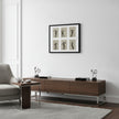 A modern living room scene featuring a dark brown wooden media console with silver metal legs, styled with decorative objects. Above it, a black-framed art print depicting six black-and-beige dance or gymnastic poses hangs on a white wall.