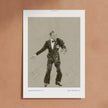 A framed art print featuring a black and white sketch of Fred Astaire in a tuxedo, displayed against a textured terracotta wall.