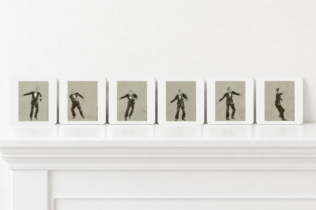 Six art print coasters arranged in a row on a white mantelpiece against a white wall. Each print shows a black-and-sepia figure posed dynamically against a muted grey background.