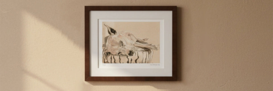 A framed art print featuring a detailed sketch of a dog, displayed on a textured beige wall with soft sunlight casting shadows.