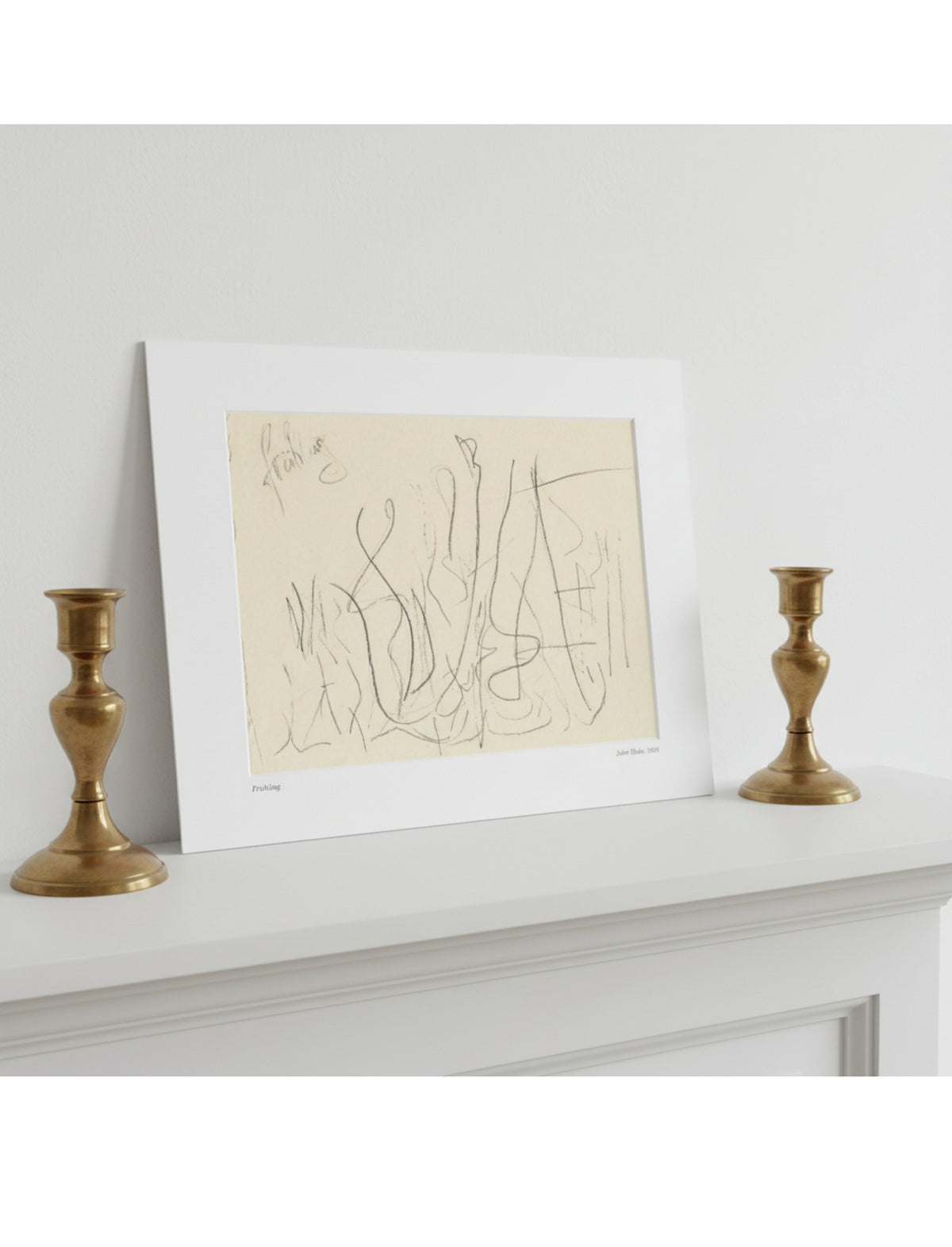 A mounted abstract line drawing in beige and black sits on a white mantelpiece, flanked by two gold candlesticks against a light gray wall.