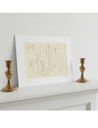 A mounted abstract line drawing in beige and black sits on a white mantelpiece, flanked by two gold candlesticks against a light gray wall.