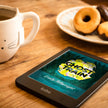 A Kobo e-reader device displaying the book cover of 'Ghost Train' ebook by Emily Tellwright, placed on a wooden table next to a white ceramic mug and a plate of donuts.