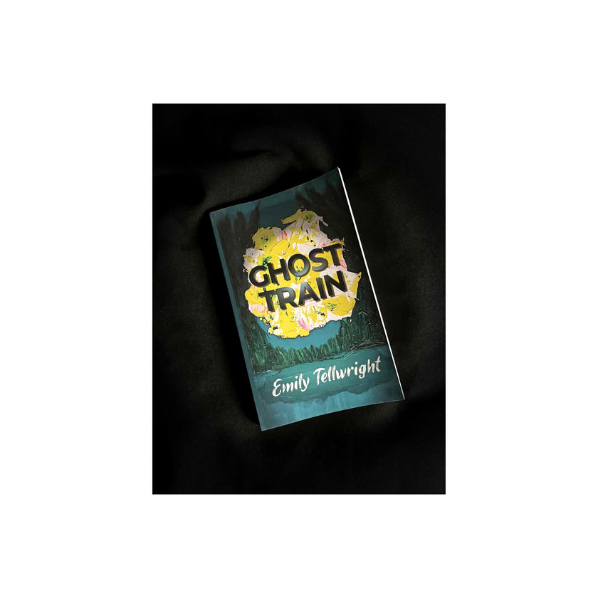 The book cover of 'Ghost Train' by Emily Tellwright, featuring a yellow and white abstract illustration on a dark teal background, displayed on a black fabric surface.