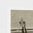 A square art print featuring a monochrome charcoal-style drawing of a figure in a dark dress, shown against a white border on a light textured background.