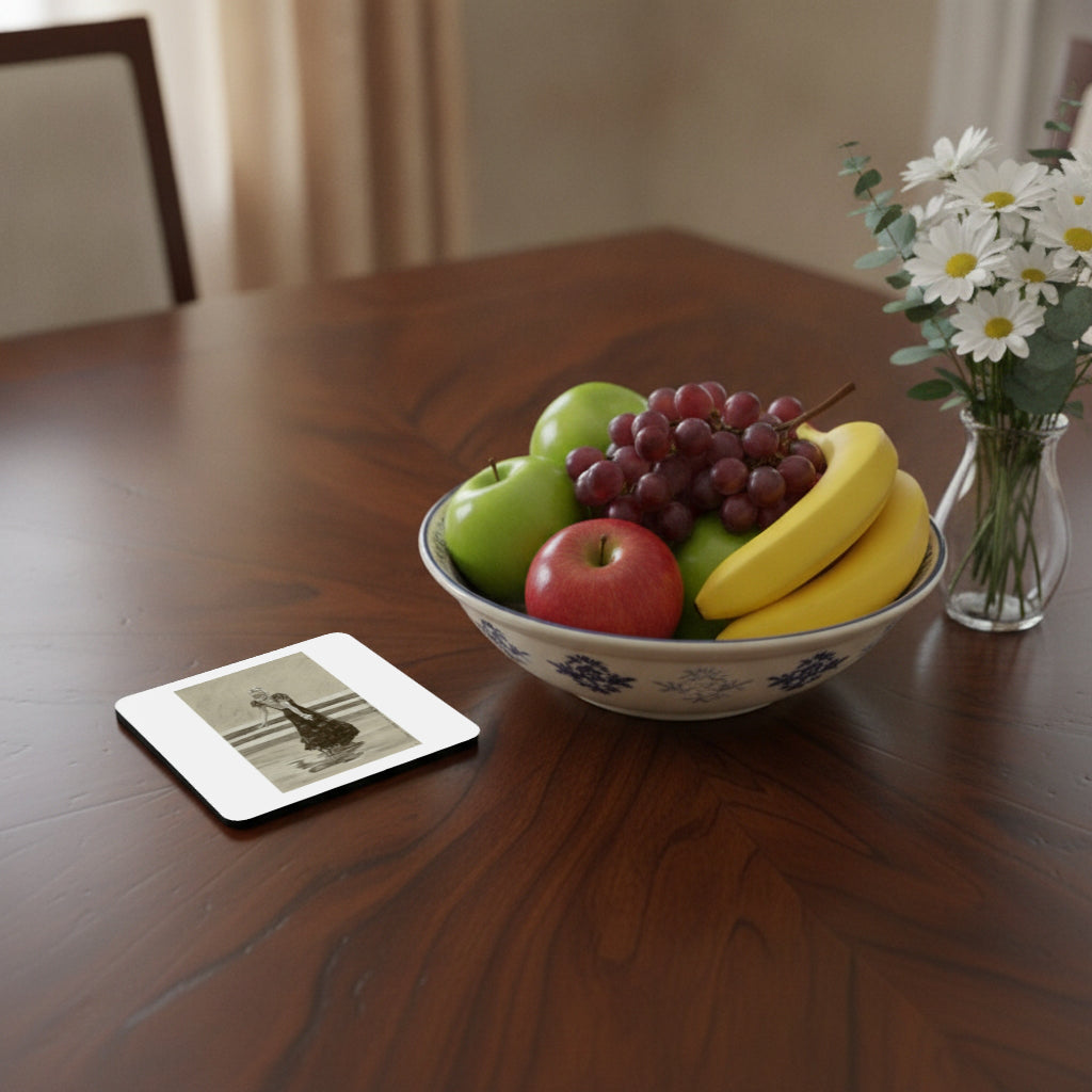 A square white coaster with a black-and-white vintage photograph lies on a polished dark wood dining table next to a ceramic bowl of fruit and a small vase of white daisies.