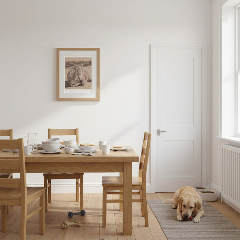 A framed art print of a drawing of a pony is on the wall above a light oak dining table with matching wooden chairs in a bright, modern dining room. A golden retriever dog is lying on a grey rug on the floor next to the table.