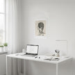 an art print of a drawing of a smoking person above a white desk with a laptop on