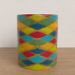 A mug with a colourful harlequin diamond pattern in red, yellow, green, and blue, separated by gold metallic lines, set on a wooden surface against a white wall.