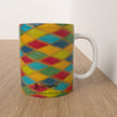 A ceramic mug with a colorful harlequin diamond pattern in yellow, blue, red, and green, sitting on a light wood tabletop against a white wall. The mug features printed text at the bottom reading 'Castle Setter Press' and 'Harlequin & Emily Tellwright, 2021'.