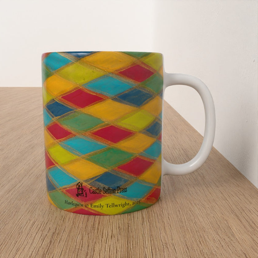 A ceramic mug with a colorful harlequin diamond pattern in yellow, blue, red, and green, sitting on a light wood tabletop against a white wall. The mug features printed text at the bottom reading 'Castle Setter Press' and 'Harlequin & Emily Tellwright, 2021'.