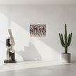 A black and white art print hanging on a white wall in a styled living room setting with a dark gray leather armchair, a wooden side table, a potted plant, and a floor lamp.