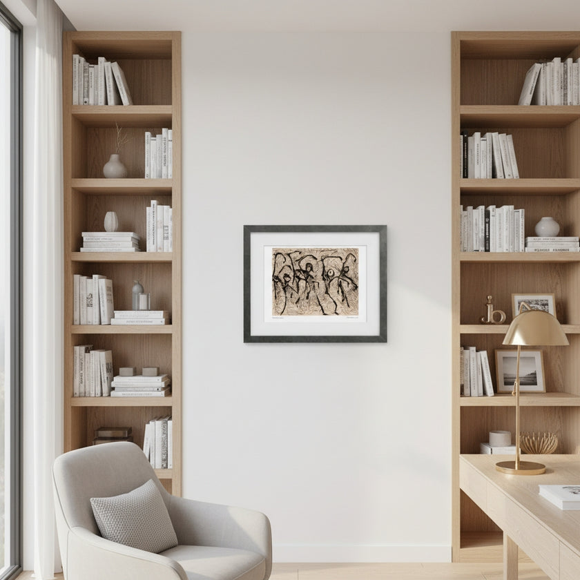 A framed art print featuring black ink figures on a beige background, displayed in a black frame on a white wall between two tall wooden bookshelves in a modern home office setting.