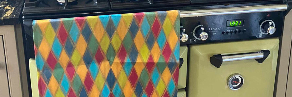 A colorful kitchen towel with a multicolor diamond pattern hanging on a cream-colored vintage-style stove oven.
