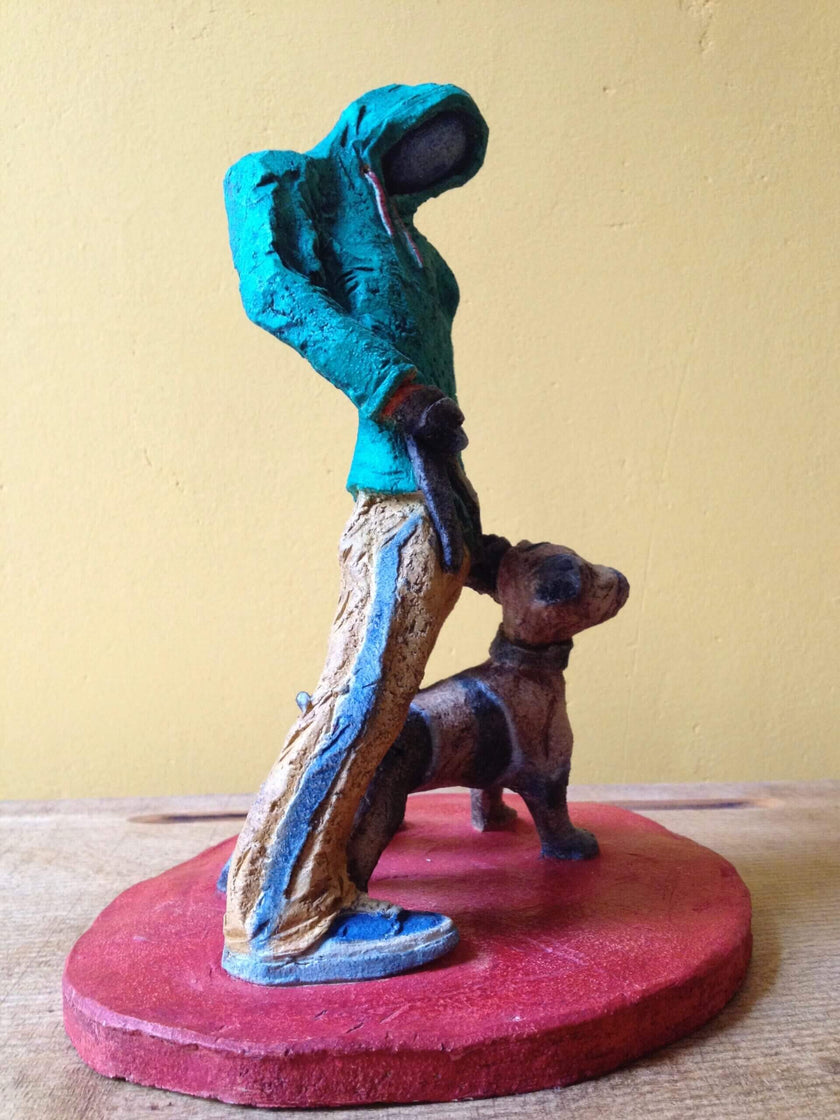 Ceramic sculpture of figure in green hoodie with a Staffordshire bull terrier on a lead.