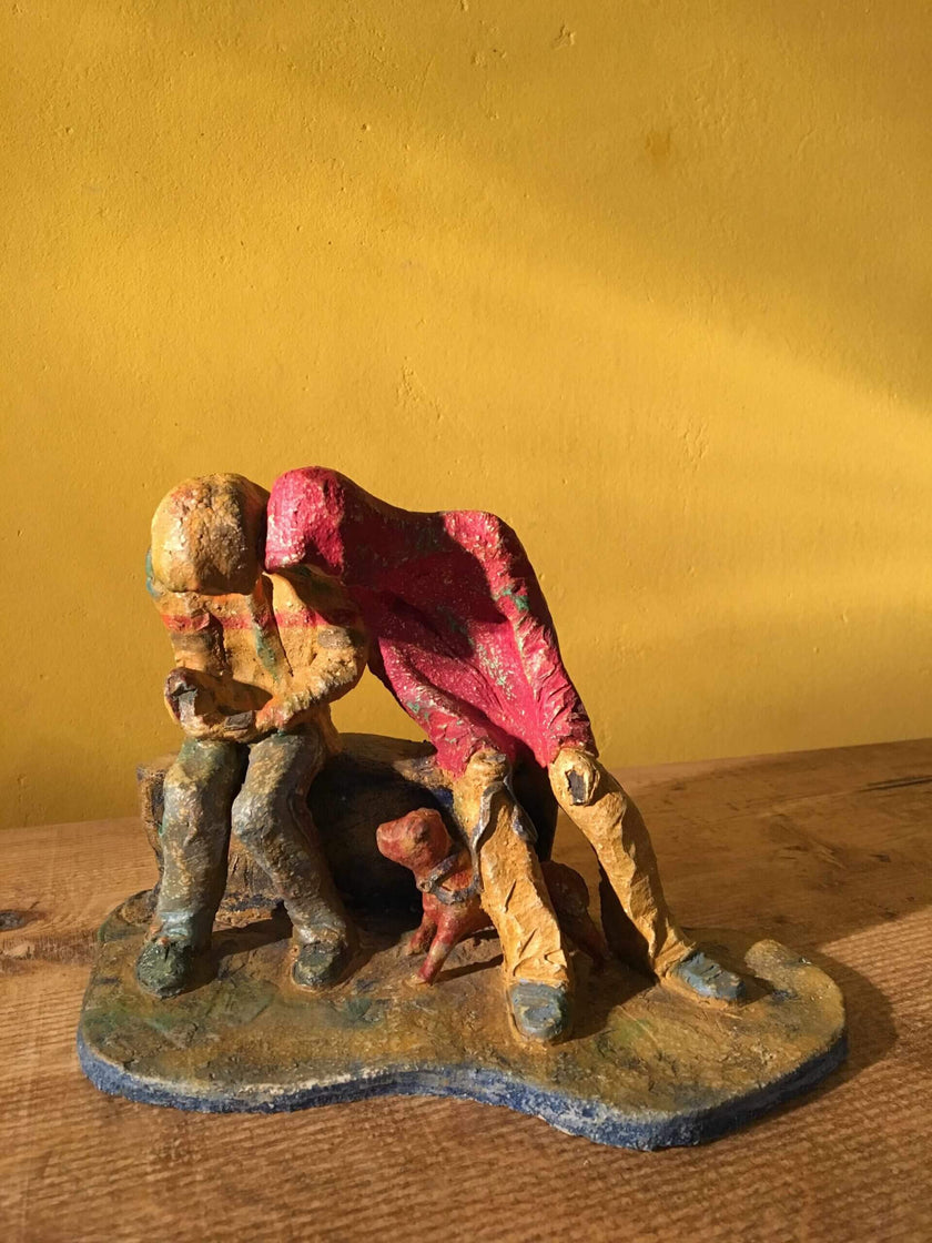Ceramic sculpture of two figures sitting in hoodies looking at mobile phones with a dog at their feet.