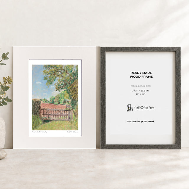 A  landscape art print displayed next to a frame insert showing product details. The print depicts a green country scene with a wooden fence under a blue sky, set in a white mat inside a white frame.