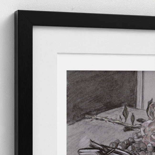 Close-up of a framed wall art print with a black frame, white mat, and a monochrome still-life drawing showing fruit and branches.