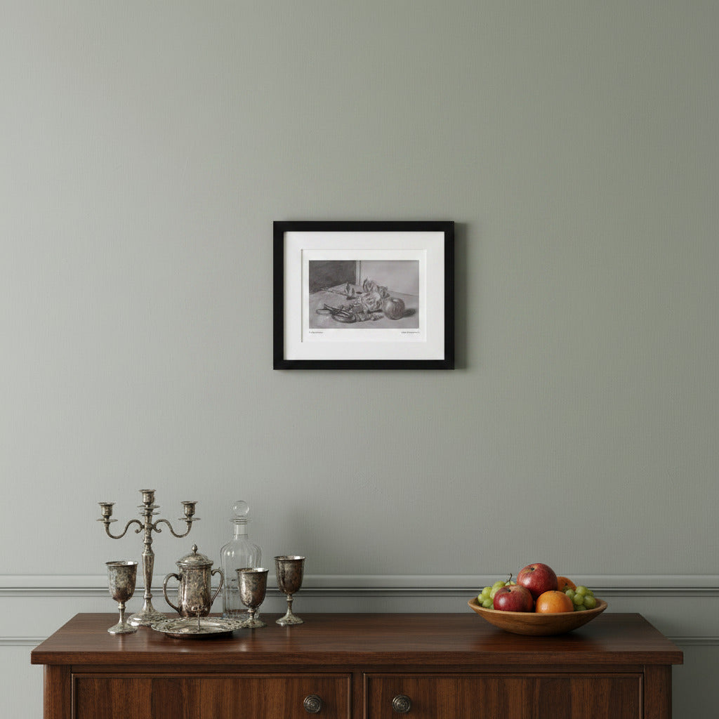 A framed black and white still life art print hangs on a light gray wall above a dark wood sideboard with silver goblets, a glass decanter, and a bowl of fruit.