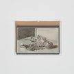 A card featuring a monochrome still life sketch of flowers, fruit, and a pair of nutcrackers, mounted on a brown kraft envelope against a light gray background.