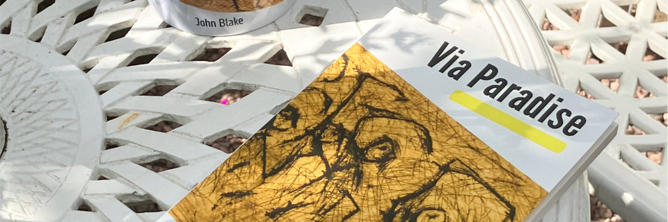 A book titled 'Via Paradise' with a gold and black abstract cover design, resting on a white lattice-patterned outdoor table.