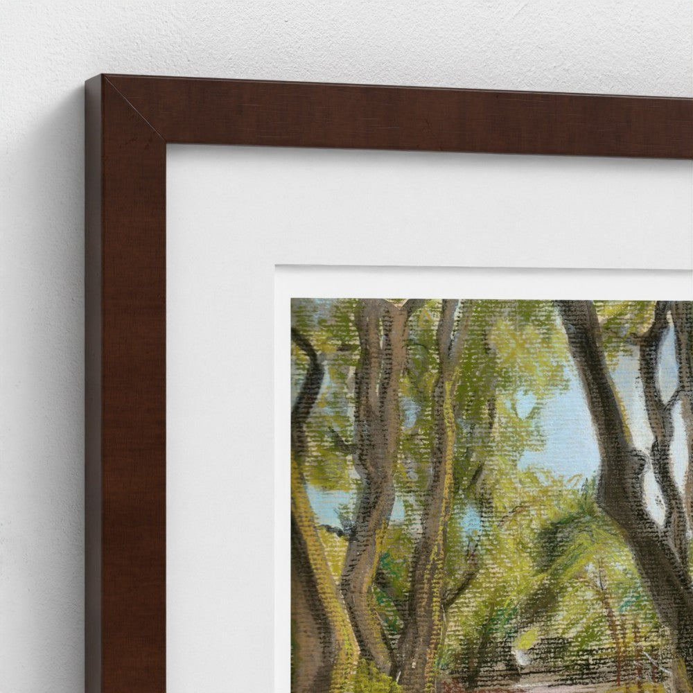 A close-up of a framed art print showing a painted forest scene with green and yellow foliage, a white mat, and a dark brown wooden frame against a white wall.