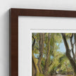A close-up of a framed art print showing a painted forest scene with green and yellow foliage, a white mat, and a dark brown wooden frame against a white wall.
