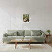 a landscape art print on a white wall above a green sofa and wood coffee table