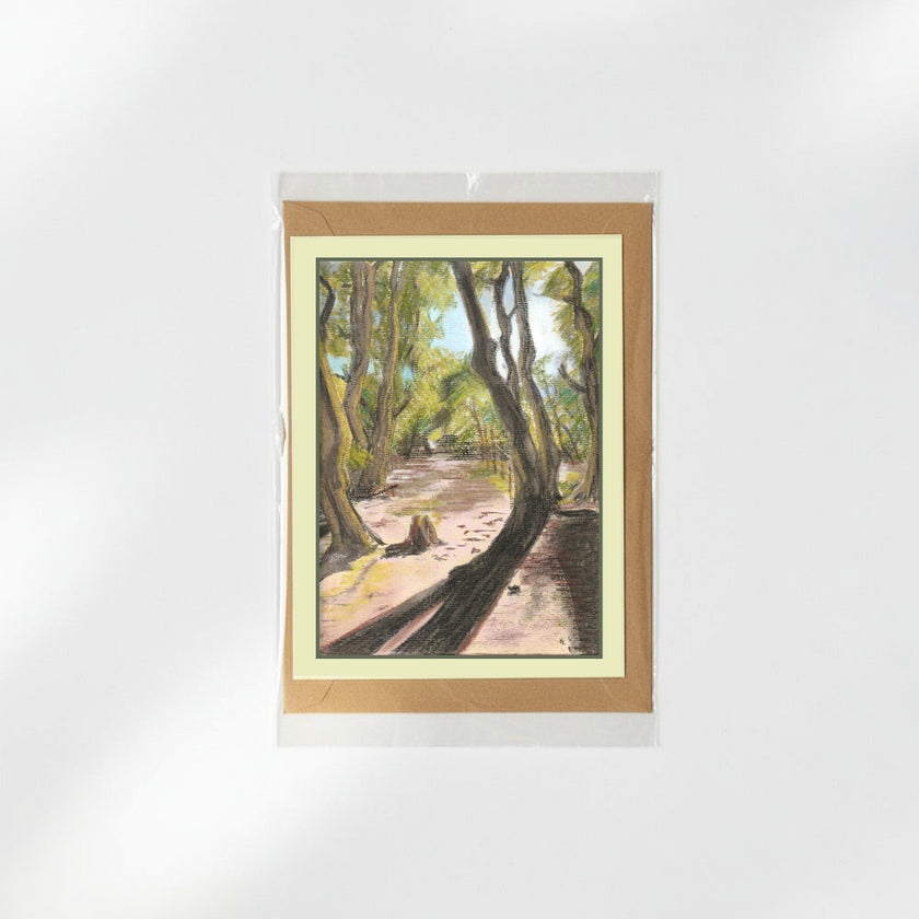 A greeting card featuring a painted forest path scene, presented in a clear sleeve with a kraft envelope behind it on a white background.