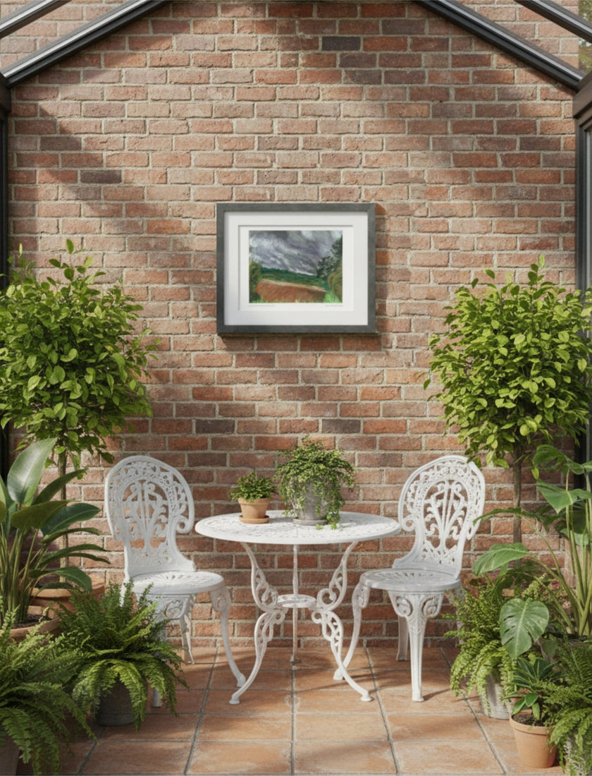 Summer Storm Near Witley Court Framed Art Print on a brick wall above white iron garden furniture with plants