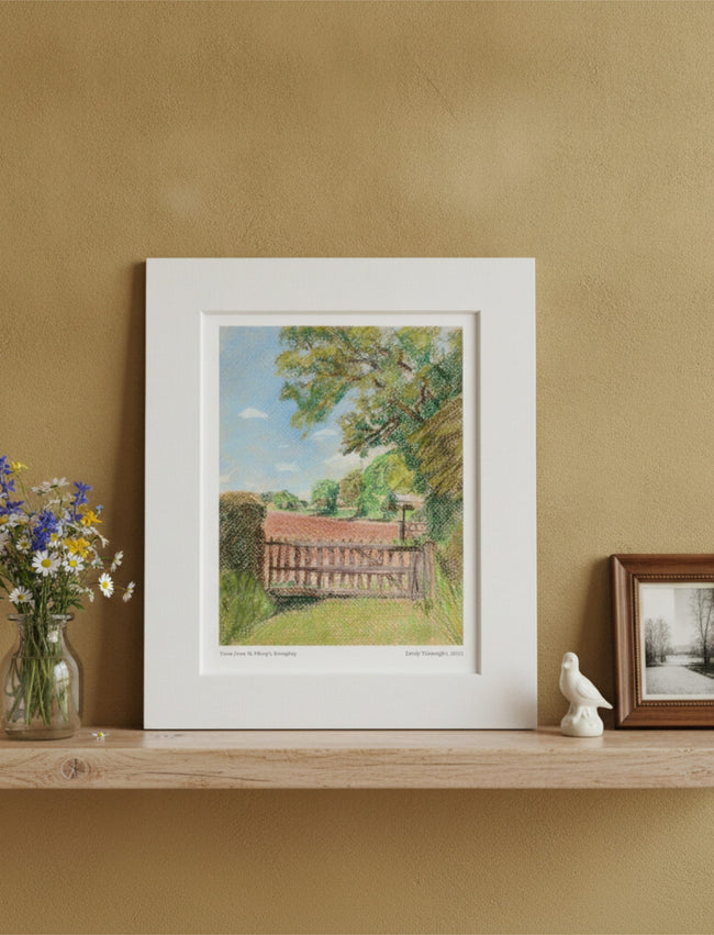 The View from St Mary's Kempley Mounted Art Print on a shelf with vase of flowers, bird ornament and photo in frame