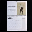 A spiral-bound April page from a vintage art calendar, featuring a black-and-white illustration of a dancer and text about Ginger Rogers 'I'll Be Hard to Handle' by Emily Tellwright. The calendar page is photographed against a solid black background.