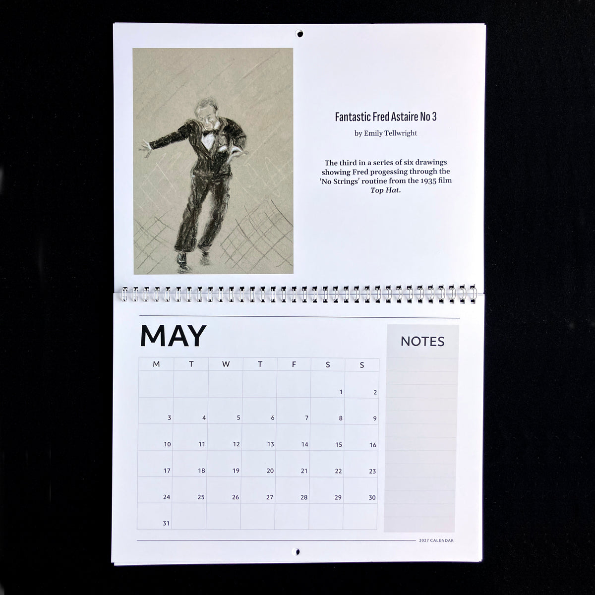 A spiral-bound May calendar page from 'Fantastic Fred Actaire No 3' by Emily tellwright, featuring a sketch of a dancer and a calendar grid with a notes section, photographed against a black background.